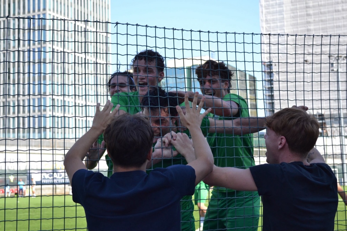 Giocatori di ASD Venticento festeggiano aggrappandosi alla rete del campo, con lo skyline di Milano sullo sfondo